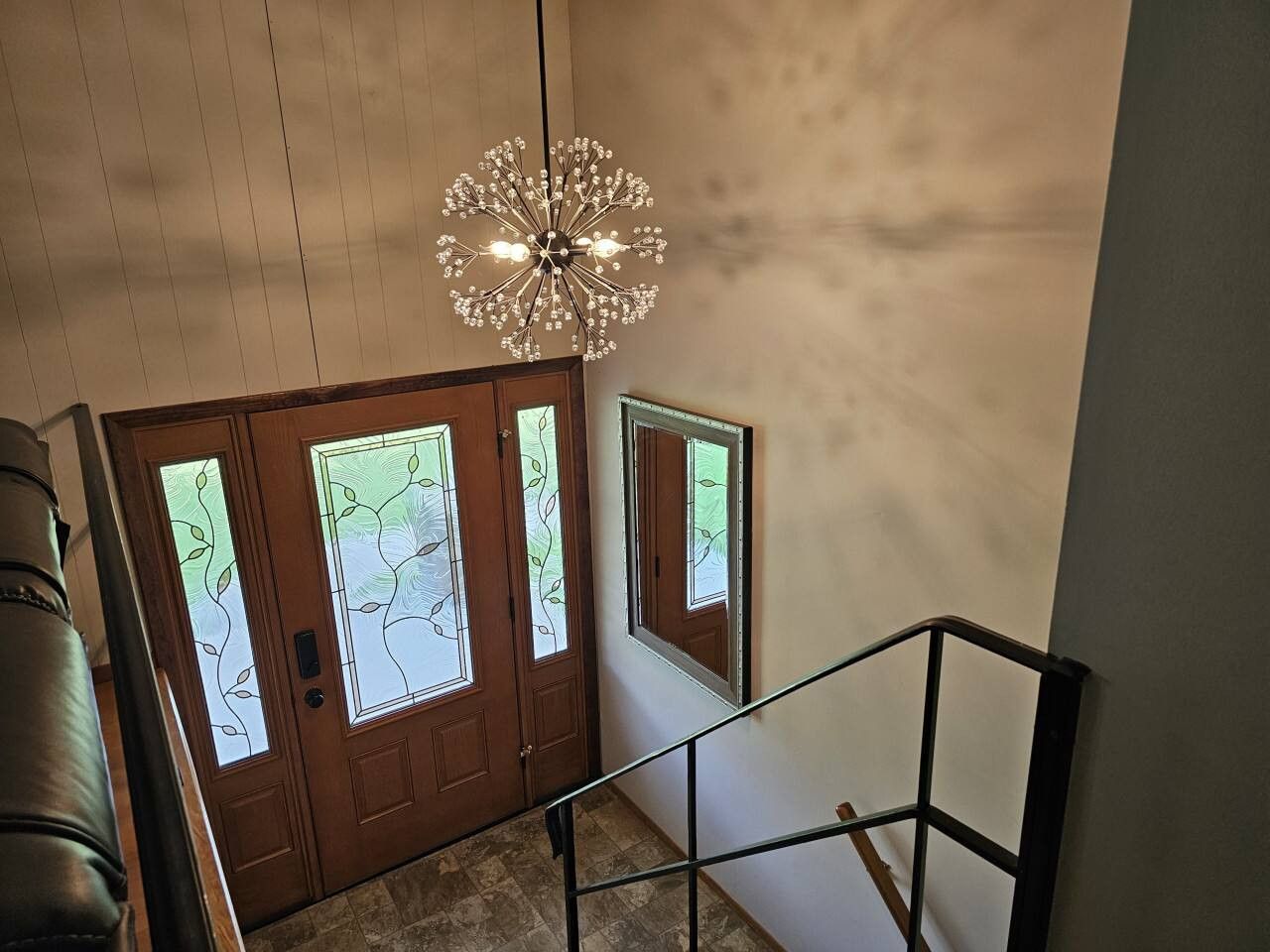 Una escalera con una lámpara moderna, puertas de madera con paneles de vidrio esmerilado y barandilla de metal.