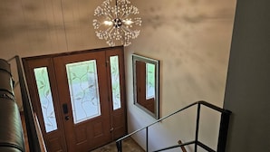Una escalera con una lámpara moderna, puertas de madera con paneles de vidrio esmerilado y barandilla de metal.