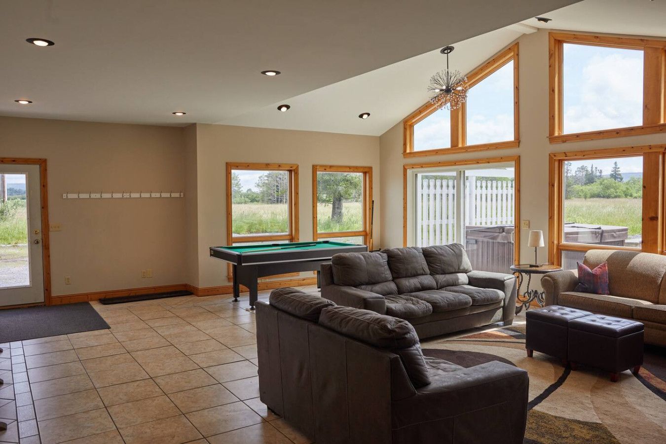 A spacious living room with a pool table, a sofa, and large windows offering views of the outdoors.