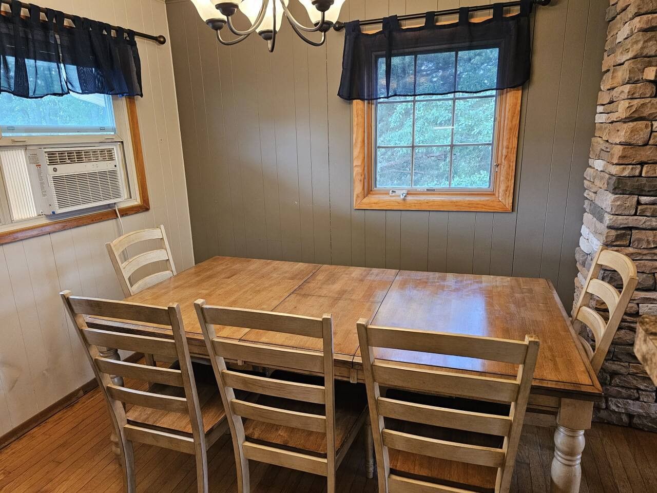 Un comedor con una mesa y sillas de madera, una araña y una pared decorativa de piedra.