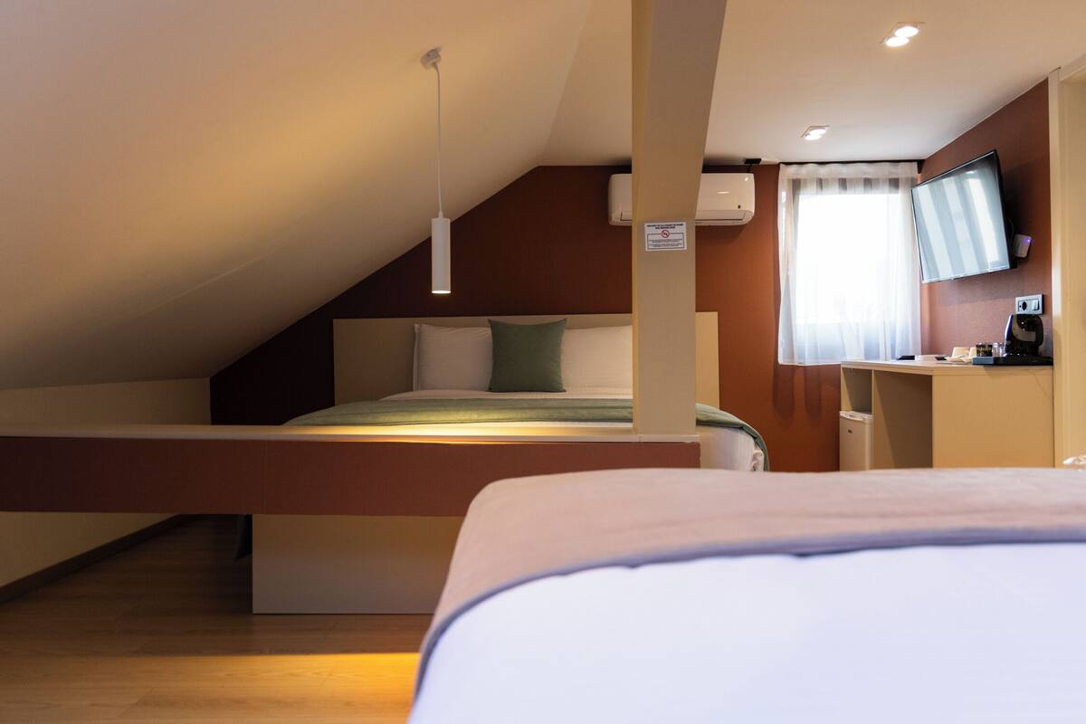 A modern hotel room with a loft bed, a desk, a flat-screen TV, and a window with curtains.
