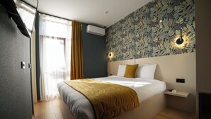 A modern bedroom with a large bed, a headboard with built-in lighting, a small bedside table, and a wall-mounted air conditioner. - Hotel Ma Belle (Pristina)