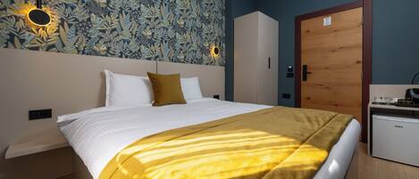 Quarto de hotel com uma cama, um guarda-roupa, uma escrivaninha e uma parede com padrão de folhagem.