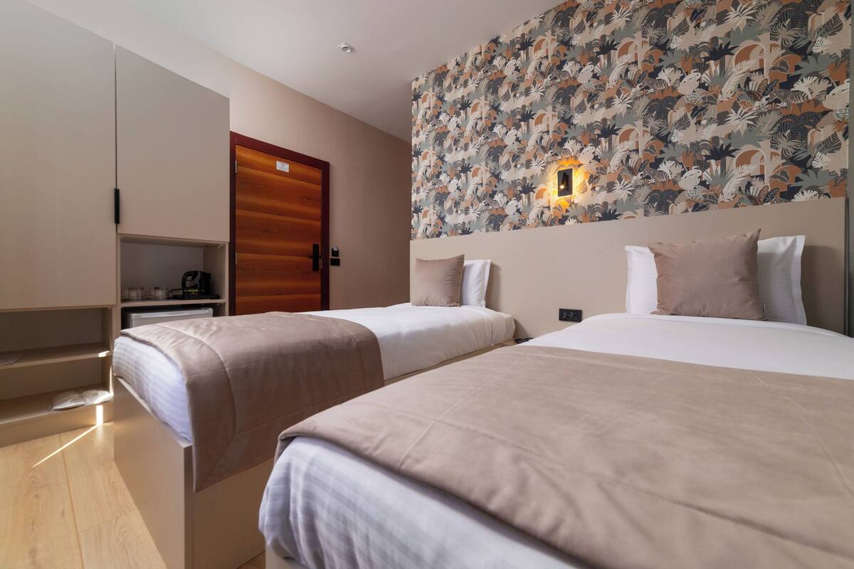 A hotel room with two beds, a wardrobe, a desk, and a patterned wall.