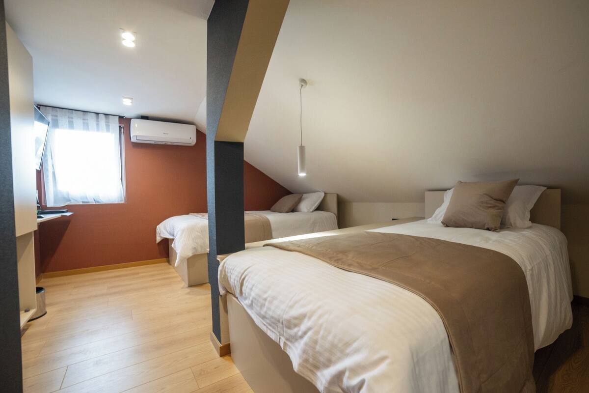 A bedroom with two beds, a desk, and an air conditioning unit.