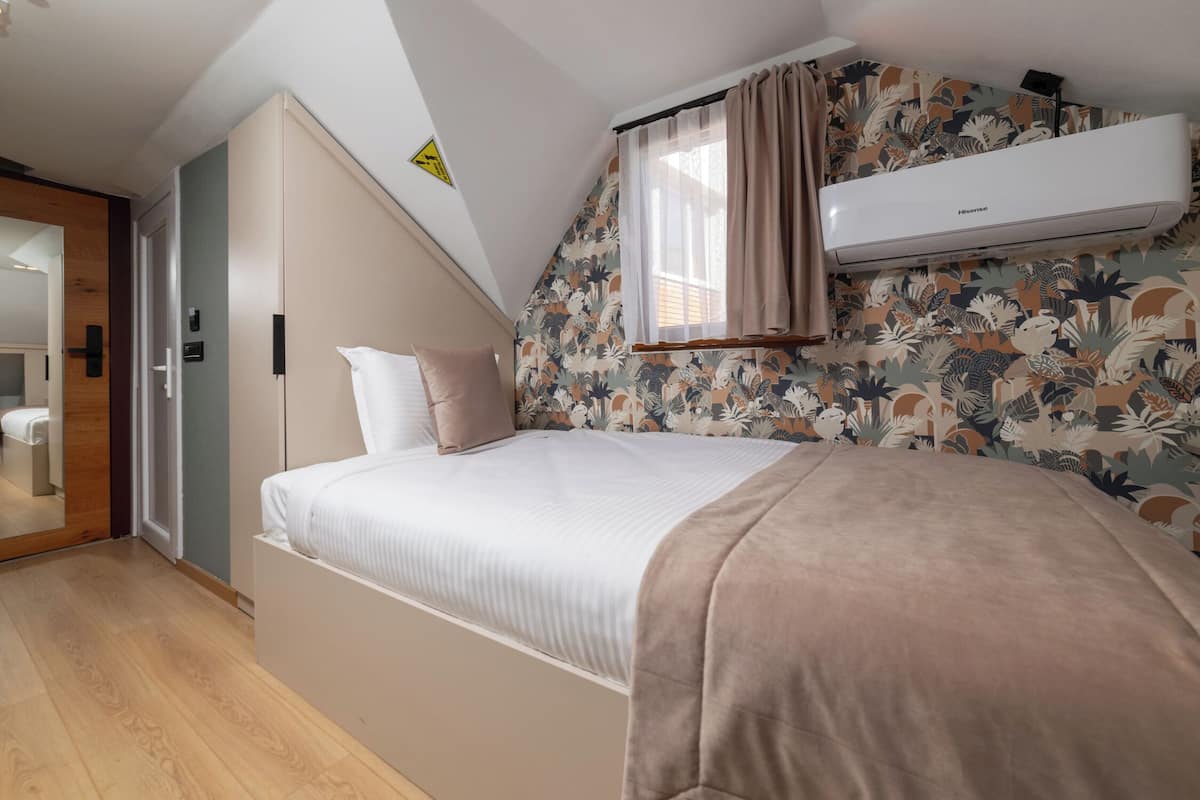 A bedroom with a bed, an air conditioner, a window with curtains, and a floral wallpaper.