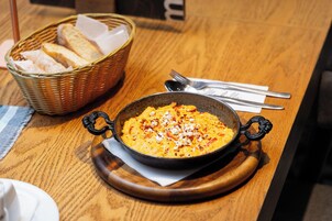Una mesa de madera con un cuenco de comida, un cesto de pan y cubiertos.