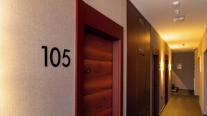 A hallway with a number '105' on the wall, wooden doors, and a carpeted floor. - Hotel Ma Belle (Pristina)