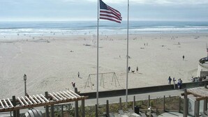 A beach with an American flag, a swing set, and a view of the ocean. - Charming 1-bedroom unit in resort with fitness room in Seaside next to boardwalk (Seaside)