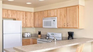 A kitchen with wooden cabinets, a microwave, a stove, a toaster, and a coffee maker. - Charming 1-bedroom unit in resort with fitness room in Seaside next to boardwalk (Seaside)