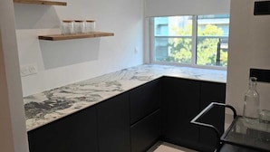 A modern kitchen with black cabinets, a marble countertop, and a window providing natural light. - Apartment Henri Martin, Trocadero, luxury and chic, Eiffel Tower view (Paris)