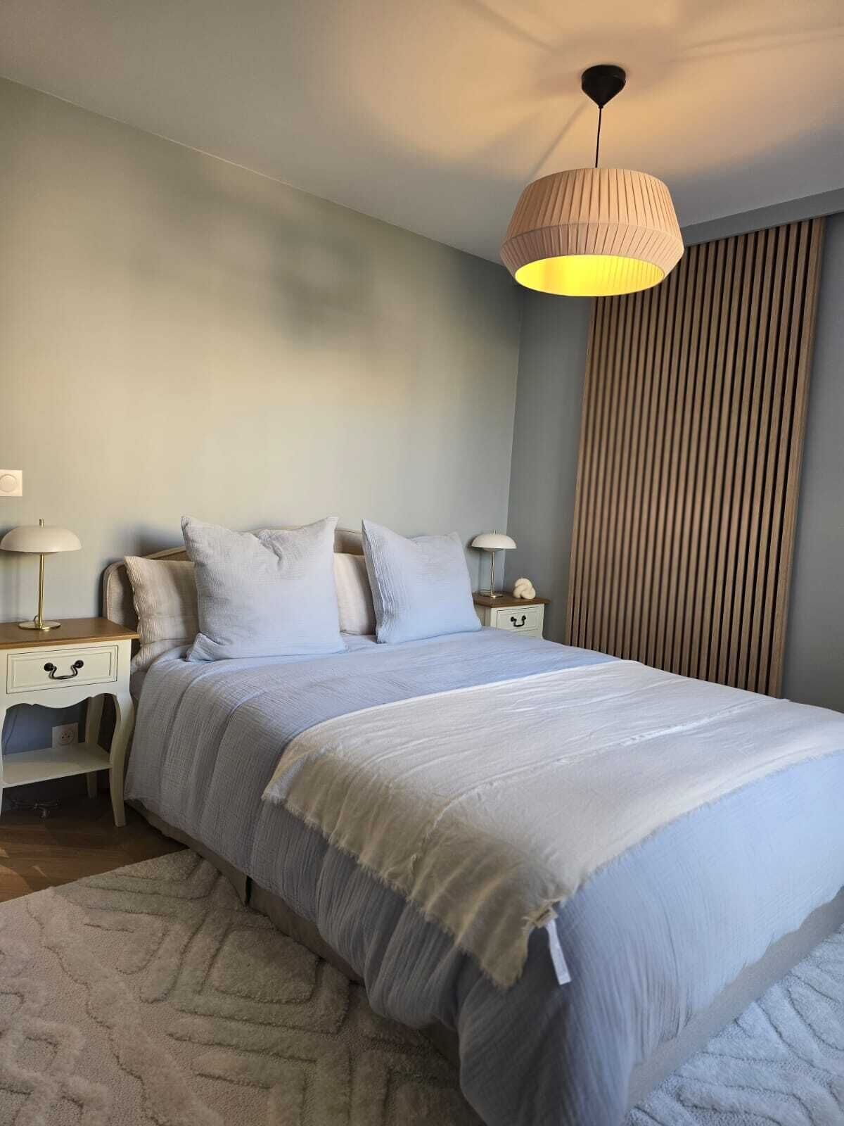 A bedroom with a bed, bedside tables, lamps, and a large window with blinds.