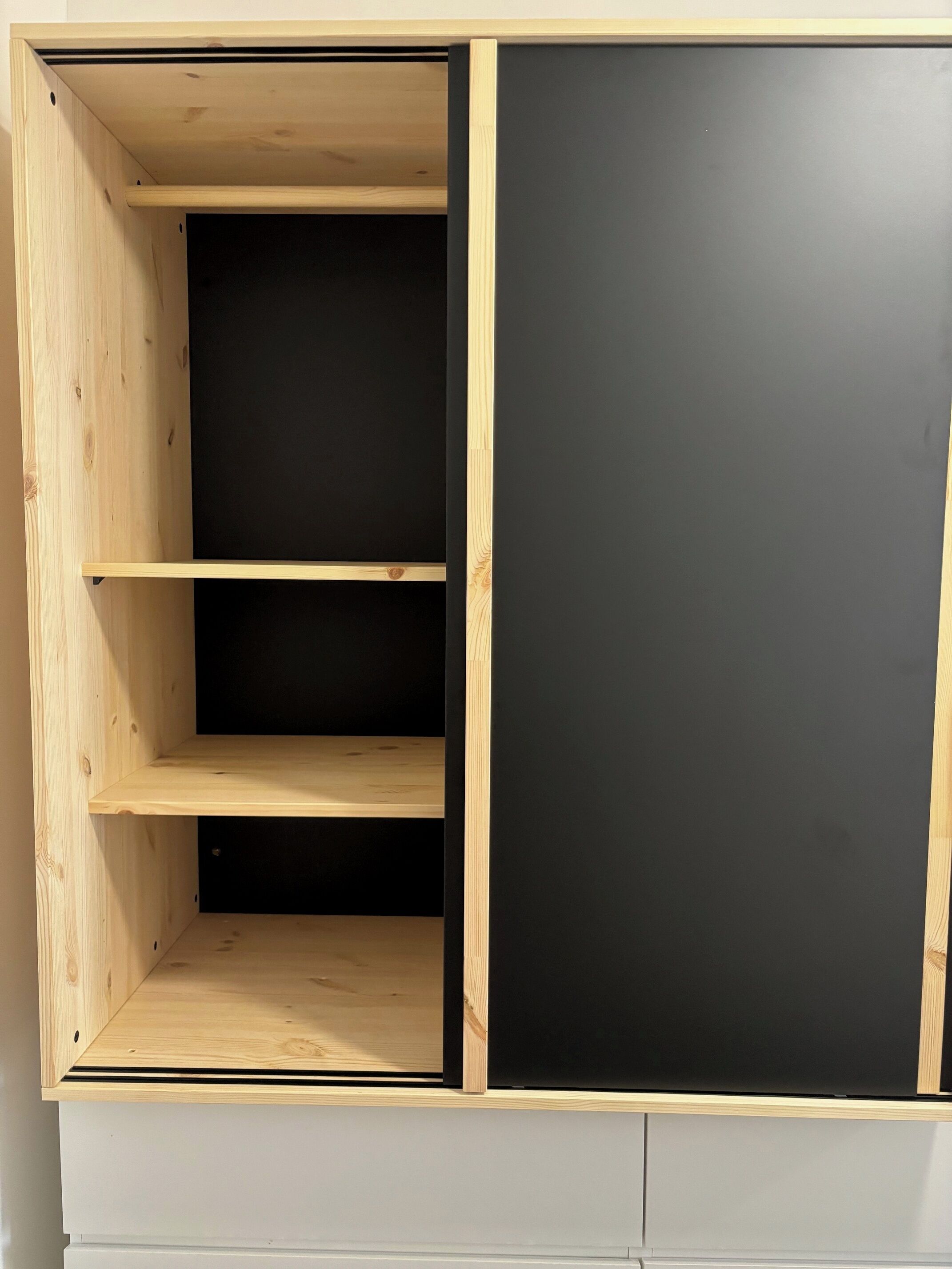 Et træskab med tre hylder og en sort panel.