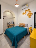 A modern bedroom with a teal bedspread, a wooden headboard, and a geometric wall decoration.