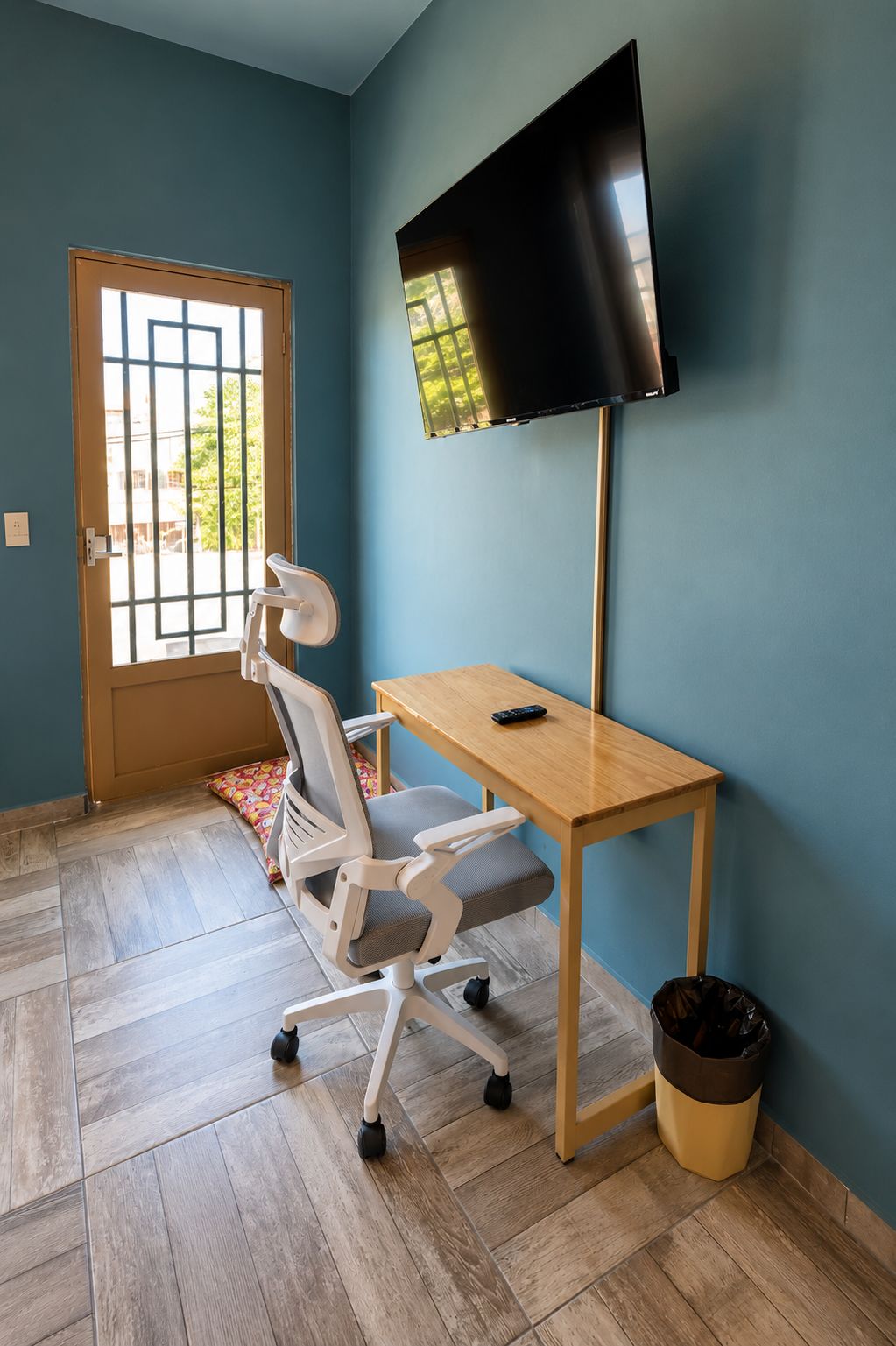 Quarto com escrivaninha, cadeira, televisão e porta com janela.