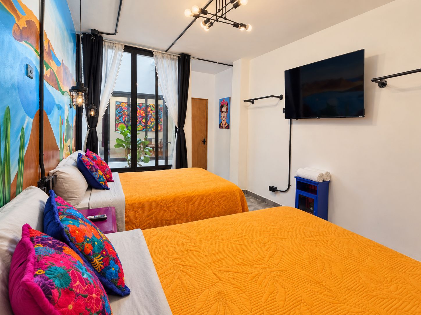 A hotel room with two beds, a TV, and a mural on the wall.
