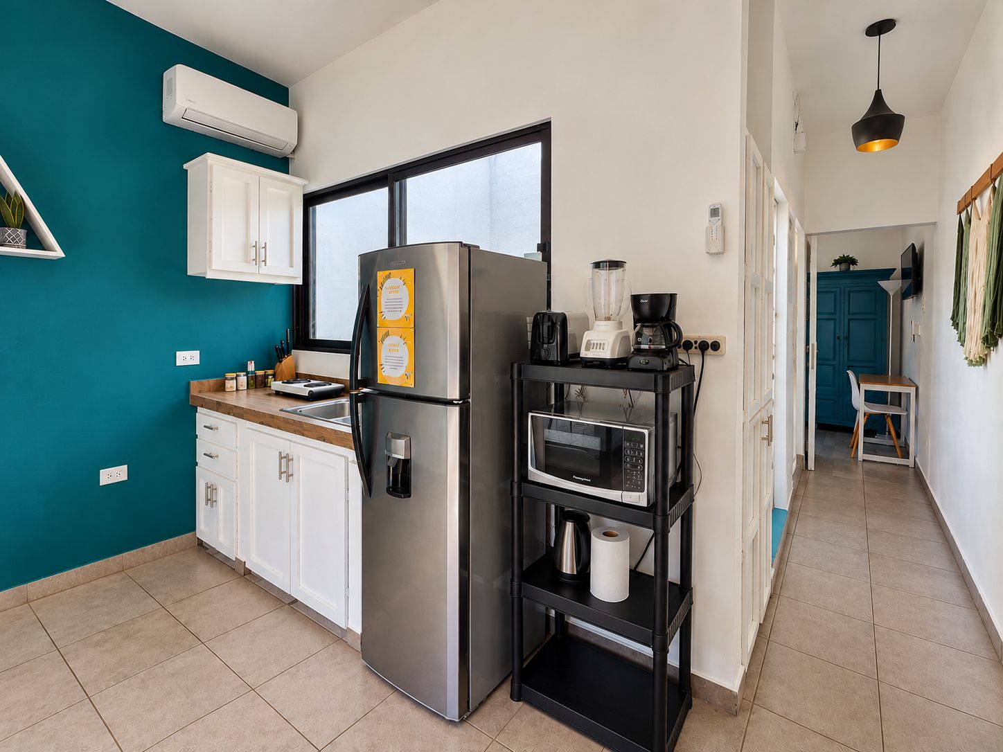 A compact kitchen with a stainless steel refrigerator, a microwave, and a coffee maker on a black shelf.
