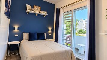 Un dormitorio con cama, mesitas de noche, lámpara en el techo, ventana con cortinas y vistas al exterior.
