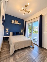 A bedroom with a bed, bedside tables, a ceiling light fixture, a window with curtains, and a view of the outside.