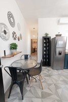 Una cocina moderna con una mesa redonda de vidrio, sillas negras, un armario negro empotrado con estantes, un refrigerador de acero inoxidable y decoración en la pared.