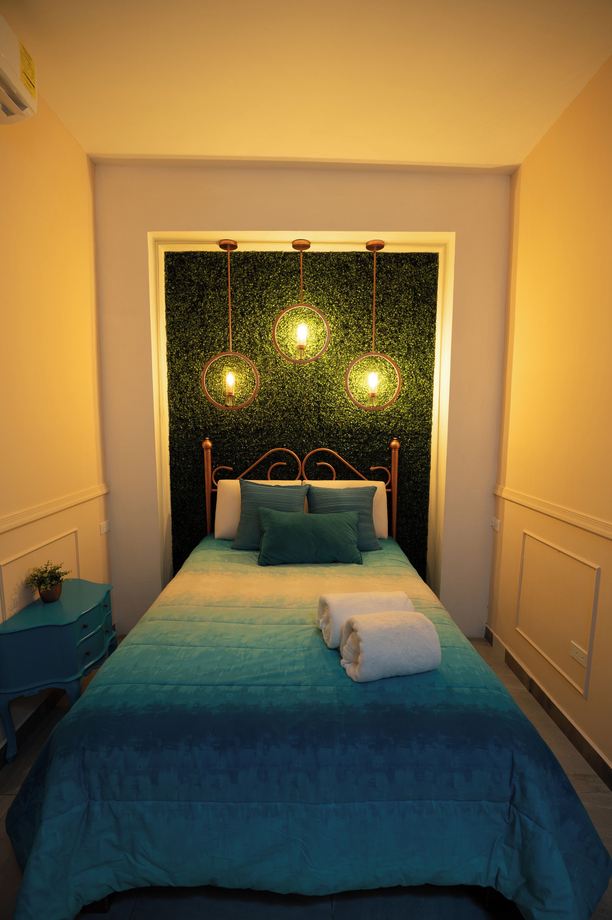 Un dormitorio con cama, mesita de noche y lámpara fijada a la pared.