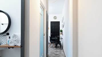 Un couloir doté d’un sol orné de motifs géométriques, une porte noire, un coin repas avec une table et des chaises, et un luminaire suspendu.