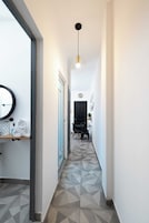 A hallway with geometric patterned flooring, a black door, a dining area with a table and chairs, and a pendant light.