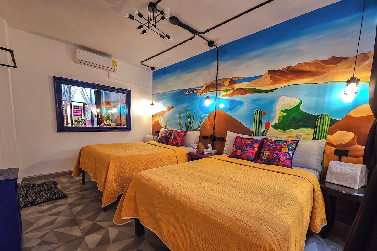 A hotel room with two beds, a large window, a mural, and a geometric patterned floor.