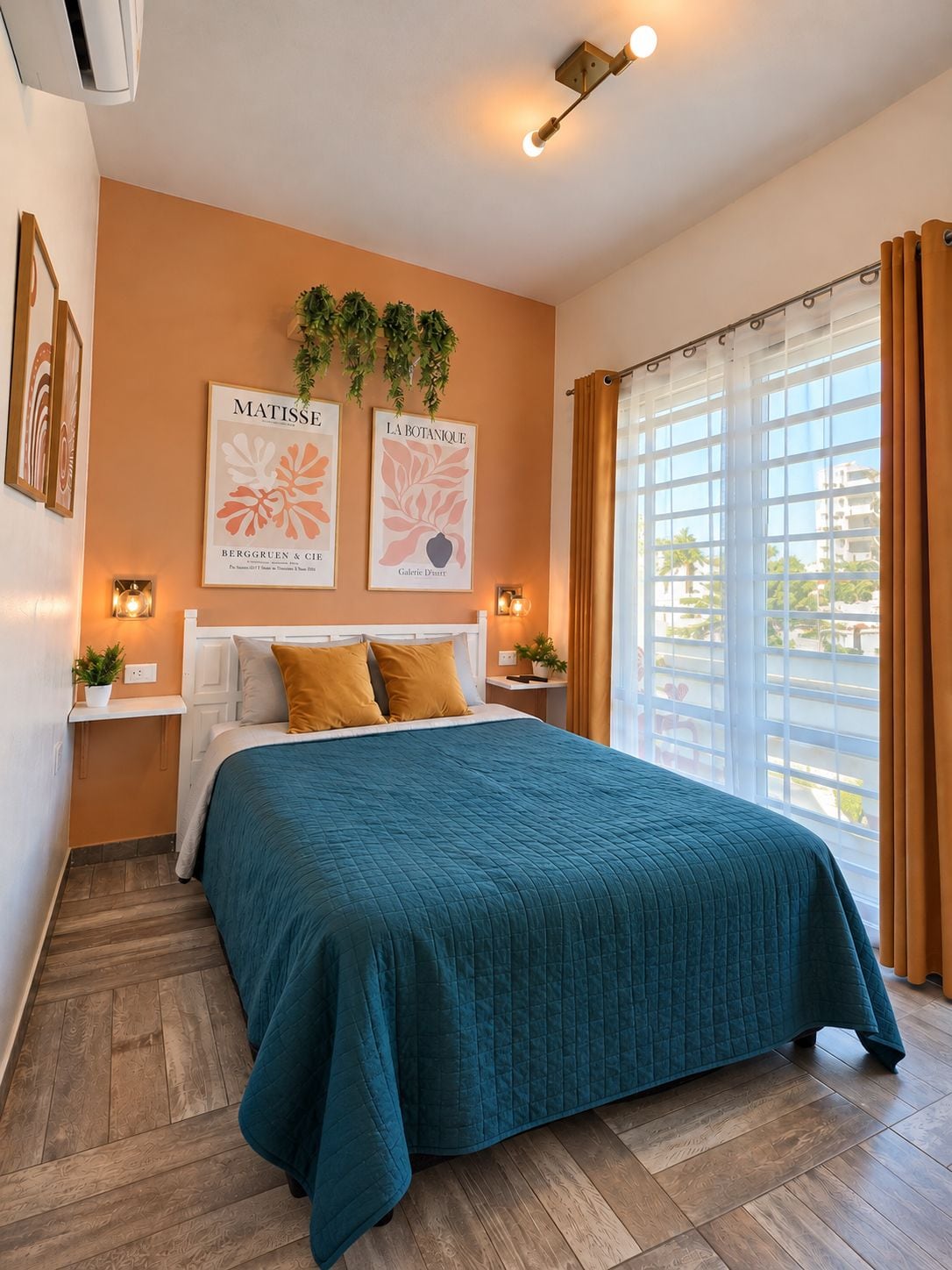 A bedroom with a large bed, two bedside tables with lamps, a window with curtains, and wall art.