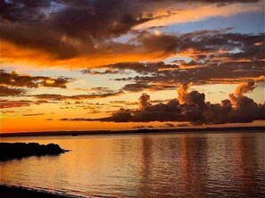 Solnedgang over stille vand med silhuet af land i det fjerne.