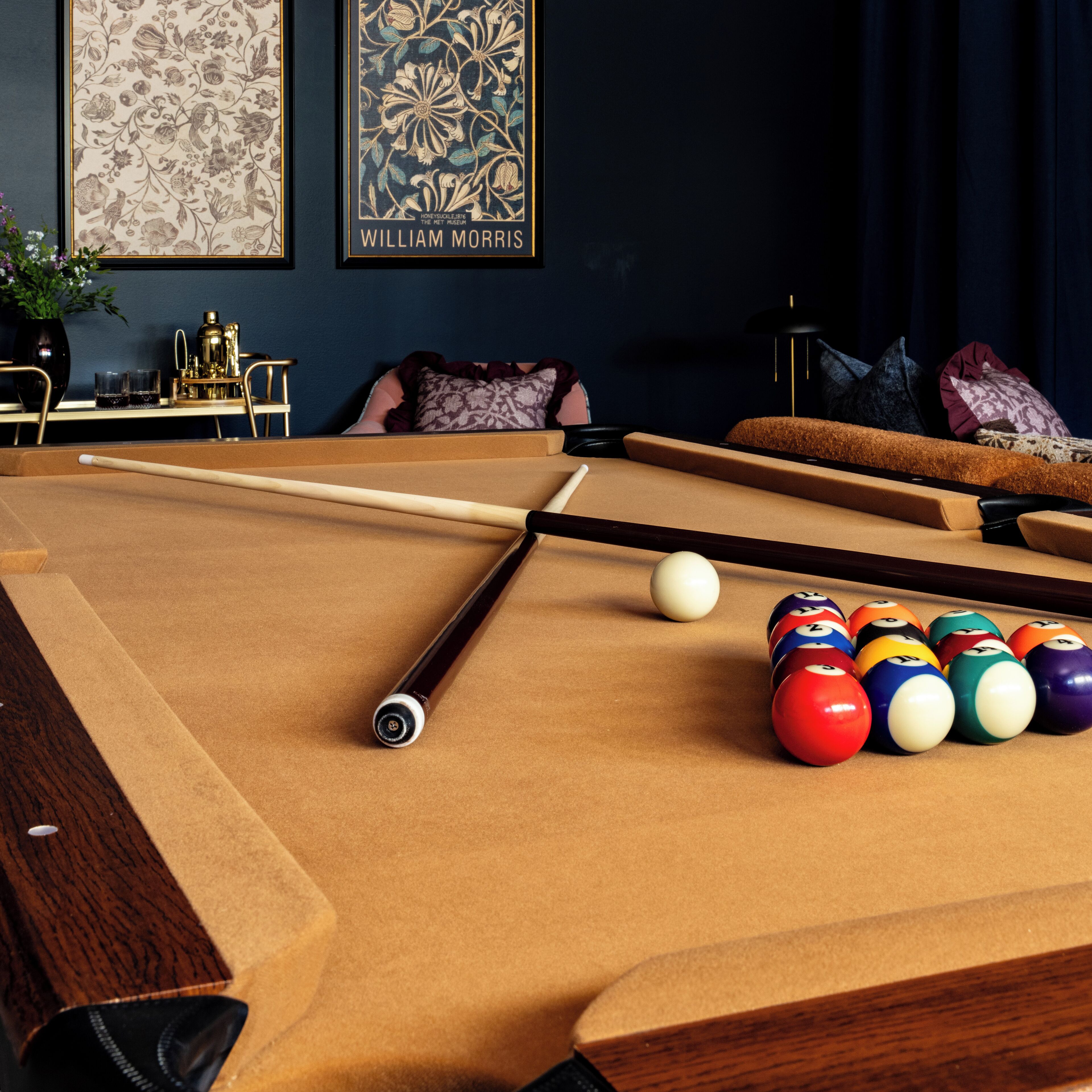A pool table with balls and cues, a sofa, and two framed artworks on the wall.
