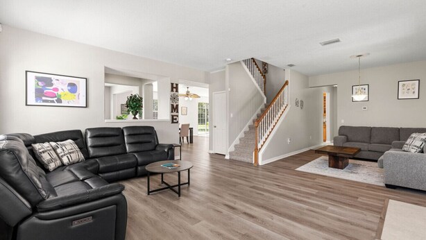 Un vaste salon comprenant un canapé en cuir noir, un canapé gris et une table basse en bois. Un escalier avec des rampes en bois mène à l’étage supérieur.