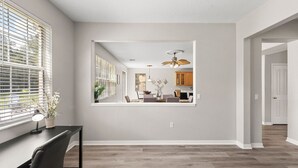Un vaste espace de vie doté d’une grande fenêtre, d’un ventilateur de plafond et offrant une vue sur la cuisine.