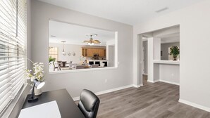Un salon moderne avec un coin repas, une cuisine visible à travers un grand miroir et un couloir menant à une autre pièce.