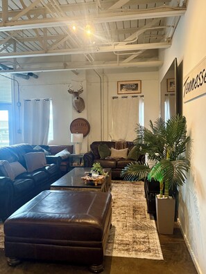 A living room with a brown leather sofa, a coffee table, and a large potted plant.