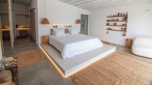 Une chambre à coucher moderne au design minimaliste, comprenant un grand lit, un banc intégré et une étagère murale agrémentée d'objets décoratifs.