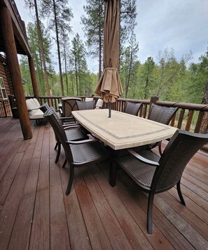 Een houten terras met een tafel en stoelen, omgeven door hoge bomen.