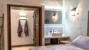Une chambre à coucher avec un lit, une porte en bois, une salle de bain avec un lavabo et un miroir, et un porte-serviettes.