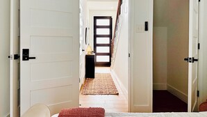 Un couloir avec un lit au fond, une porte avec un interrupteur et un tapis à motifs sur le sol.