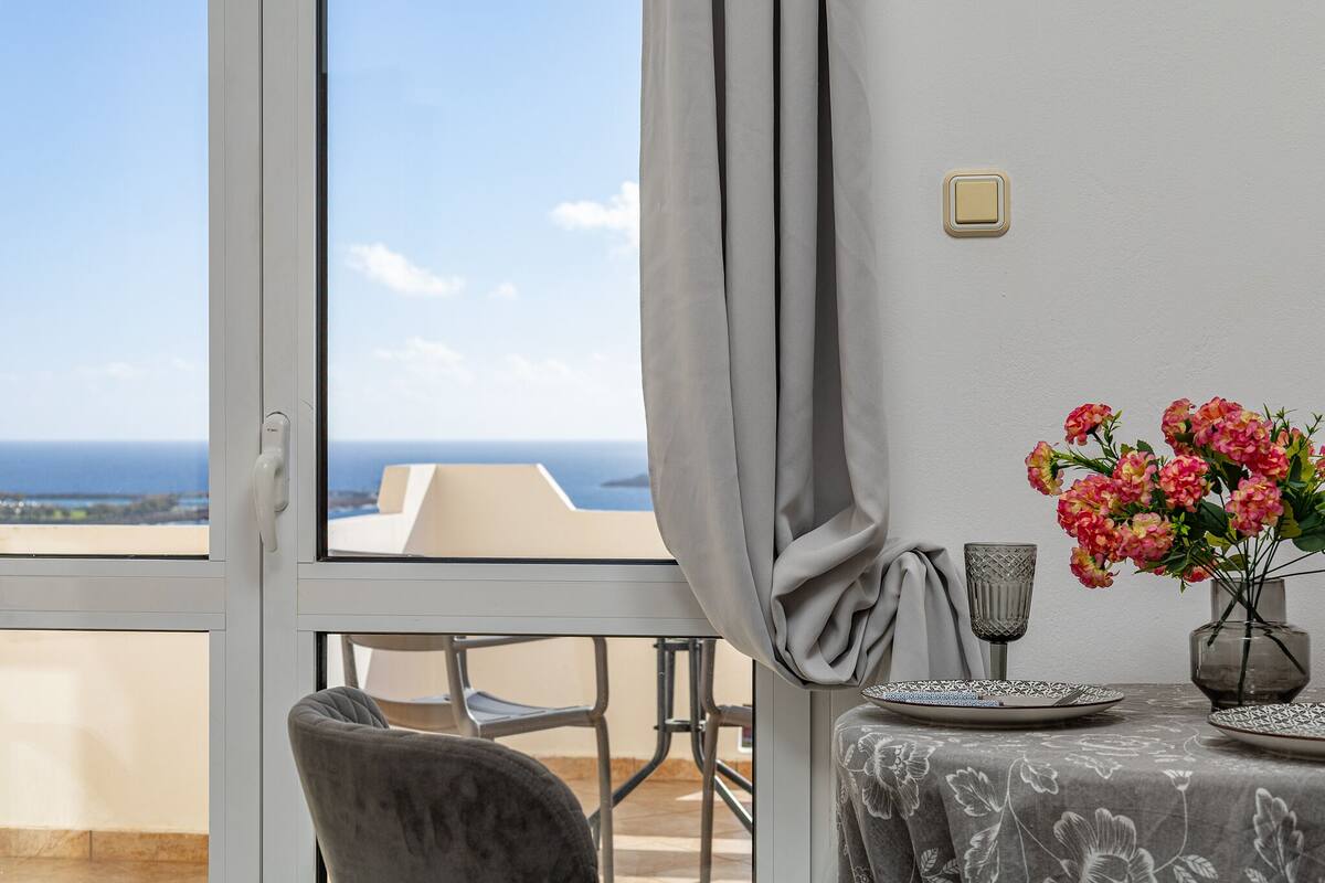 Ein Balkon mit Tisch für zwei Personen, einem Stuhl, einer Blumenvase und Blick aufs Meer.