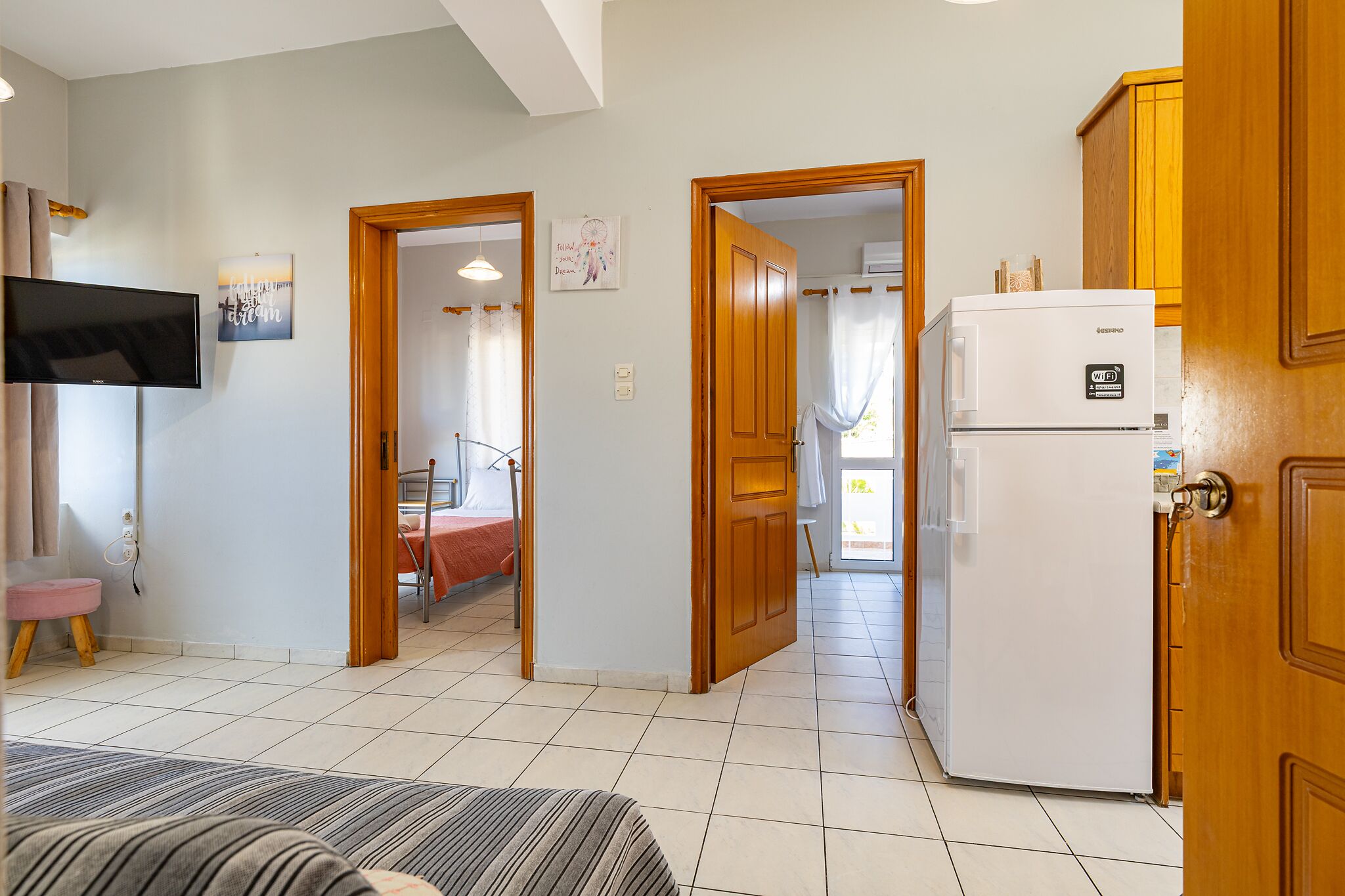 A hotel room with a bed, a TV, a refrigerator, and wooden doors leading to other rooms.