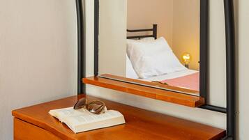 A wooden desk with a mirror reflecting a bed and a wall-mounted light fixture.