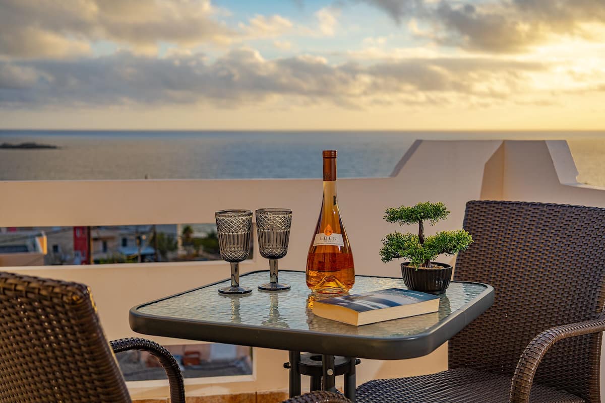 Ein Tisch mit einer Flasche, zwei Gläsern und einem Buch auf einem Balkon mit Blick auf das Meer.