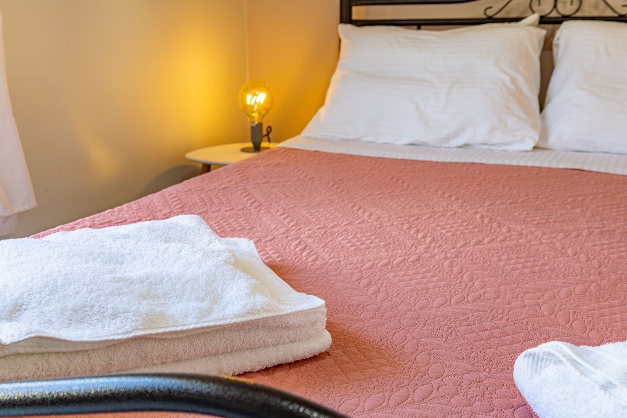 A neatly made bed with a pink quilt, white pillows, and a white towel on the side.