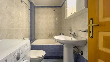 A bathroom with a bathtub, sink, toilet, and washing machine.