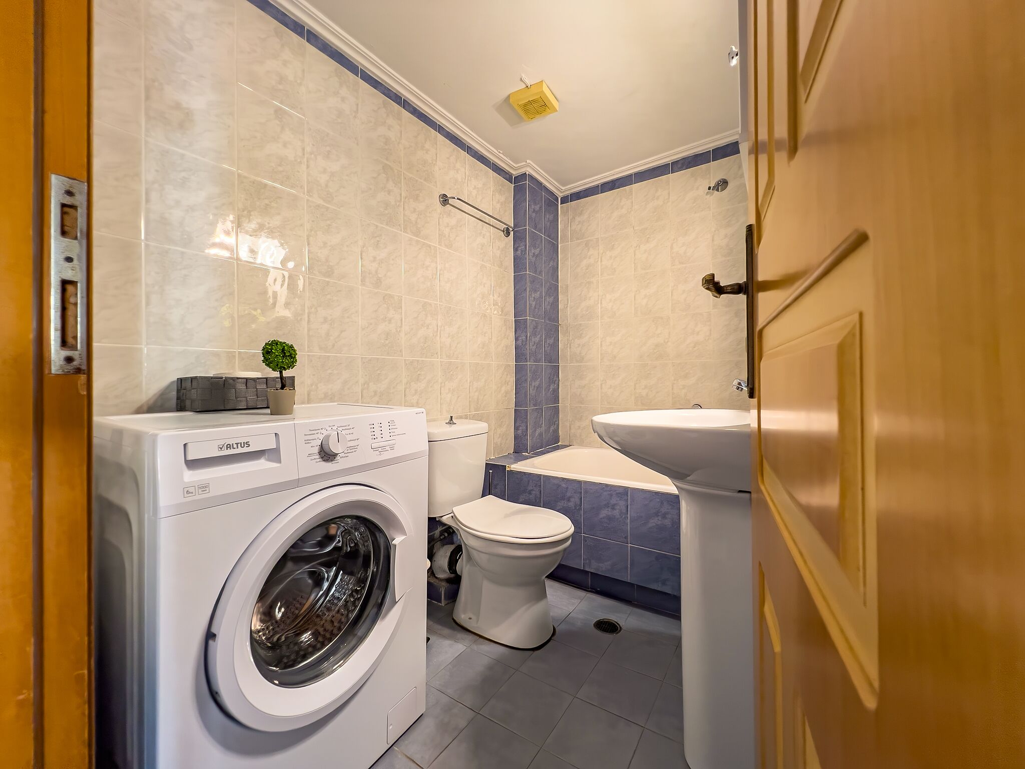 A compact bathroom with a washing machine, toilet, and sink.