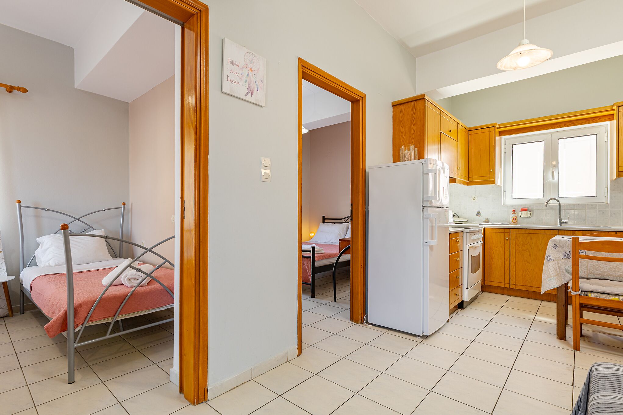 A compact hotel room with a metal bed, a kitchenette, and a bathroom visible through an open door.