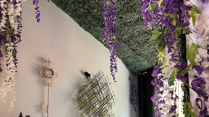 A room with a brick wall, a black refrigerator, a decorative wall clock, and a table with a chair.
