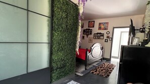 A room with a bed, a desk, and a wall covered in greenery. There are pictures on the wall and a TV on the desk.