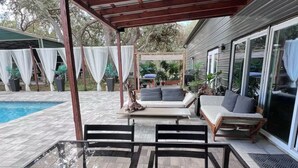 A covered outdoor seating area with a pool, cushioned seating, and a pergola structure.